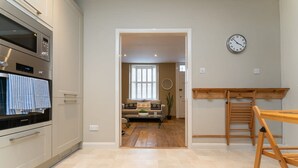 Eine moderne Küche mit eingebauten Geräten, einem Holzespeisetisch und Blick in einen Wohnbereich mit einer Couch und einem Fenster.