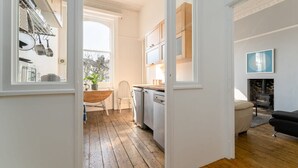 A modern kitchen with wooden flooring, a dining area with a wooden table, and a living room with a black sofa. - Host Stay Alexandra Villas (Brighton)