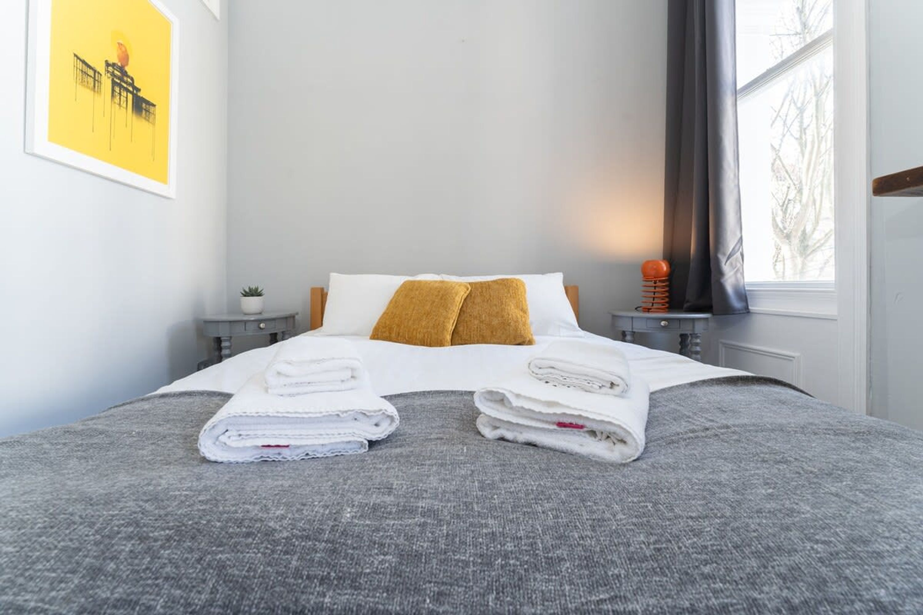 A neatly made bed with folded towels, a single pillow, and a small bedside table with a lamp.