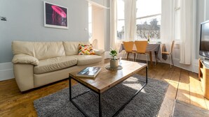 A living room with a beige sofa, a coffee table, a TV, and a dining area with chairs and a table. - Host Stay Alexandra Villas (Brighton)