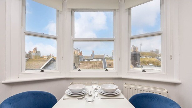 A dining area with a table set for two, large windows with a city view, and a radiator below the windows. - Host Stay Grafton Copper (Brighton)