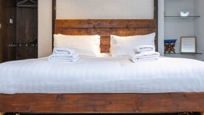 A neatly made bed with white linens and towels, a wooden headboard, and a wooden wardrobe with hangers. - Host Stay Grafton Copper (Brighton)