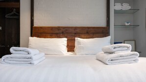 A neatly made bed with white linens and pillows, a wooden headboard, and a stack of folded towels on the side. - Host Stay Grafton Copper (Brighton)