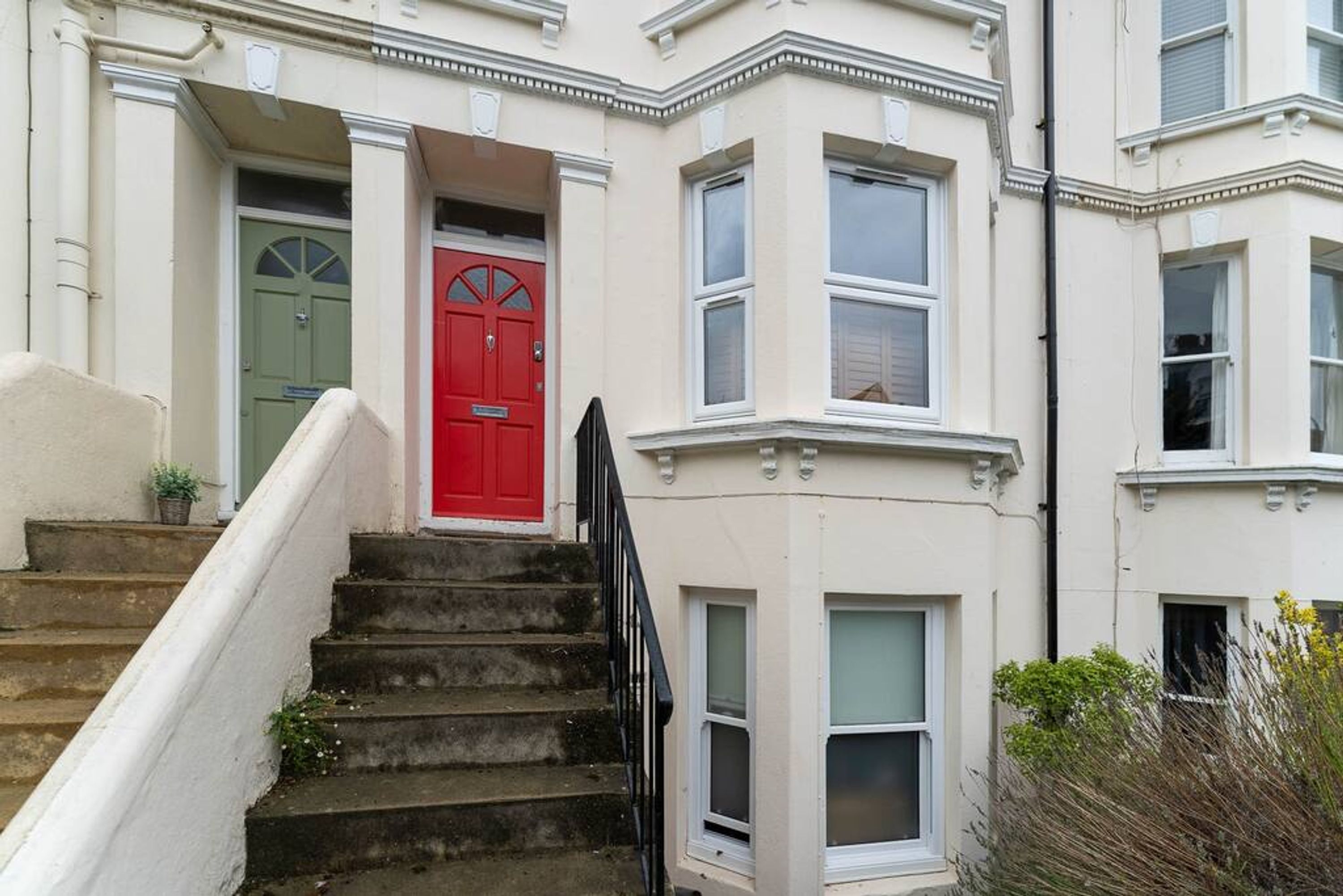 A corner house with a red door, white trim, and a set of stone steps leading to the entrance.