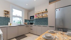 Una cocina moderna con armarios grises, una mesa de comedor de madera dispuesta con platos y vasos, y un refrigerador grande.