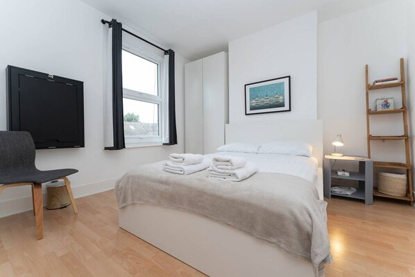 Una camera da letto moderna con un letto, una poltrona, una televisione, una finestra e uno scaffale con dei libri.