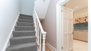 Una escalera con peldaños cubiertos de moqueta gris y balaustres blancos que conduce a una habitación con salpicadero de azulejos y armarios de madera.