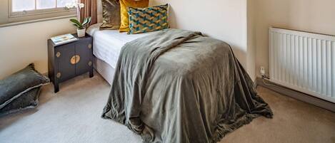 A bedroom with a bed, a bedside table, a radiator, and a window with curtains.