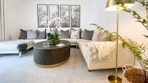 A modern living room with a white sofa, a round coffee table, and a floor lamp. There are four framed pictures on the wall. - Host Stay The Charles Street Retreat (Brighton)