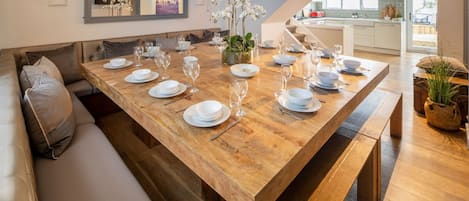 A dining area with a wooden table set for six, a sofa, and a kitchen in the background.