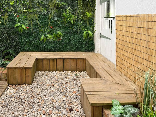 A wooden deck with a pebble ground, surrounded by dense foliage and a bamboo fence. - Host Stay The Charles Street Retreat (Brighton)
