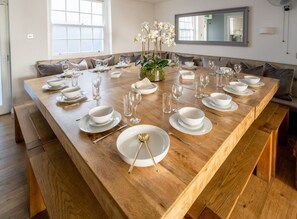 A large wooden dining table set for six with white plates, bowls, and glasses, surrounded by cushioned seating. - Host Stay The Charles Street Retreat (Brighton)