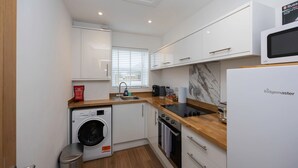 Une cuisine compacte avec des meubles blancs, un lave-linge encastré, un four à micro-ondes et un réfrigérateur.