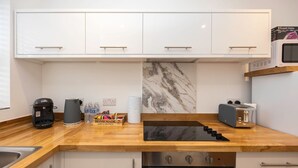 Une cuisine moderne avec des armoires blanches, un pare-feu en marbre, un four encastré, une machine à café, un grille-pain et un four à micro-ondes.