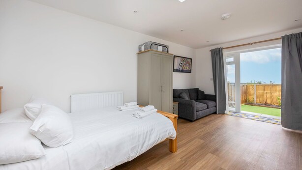 Une chambre à coucher comprenant un lit, une armoire, un canapé gris et une vue sur un jardin, accessible par une porte coulissante.