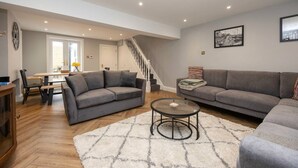 Un vaste espace de vie comprenant deux canapés gris, une table basse et un escalier menant à l’étage supérieur.
