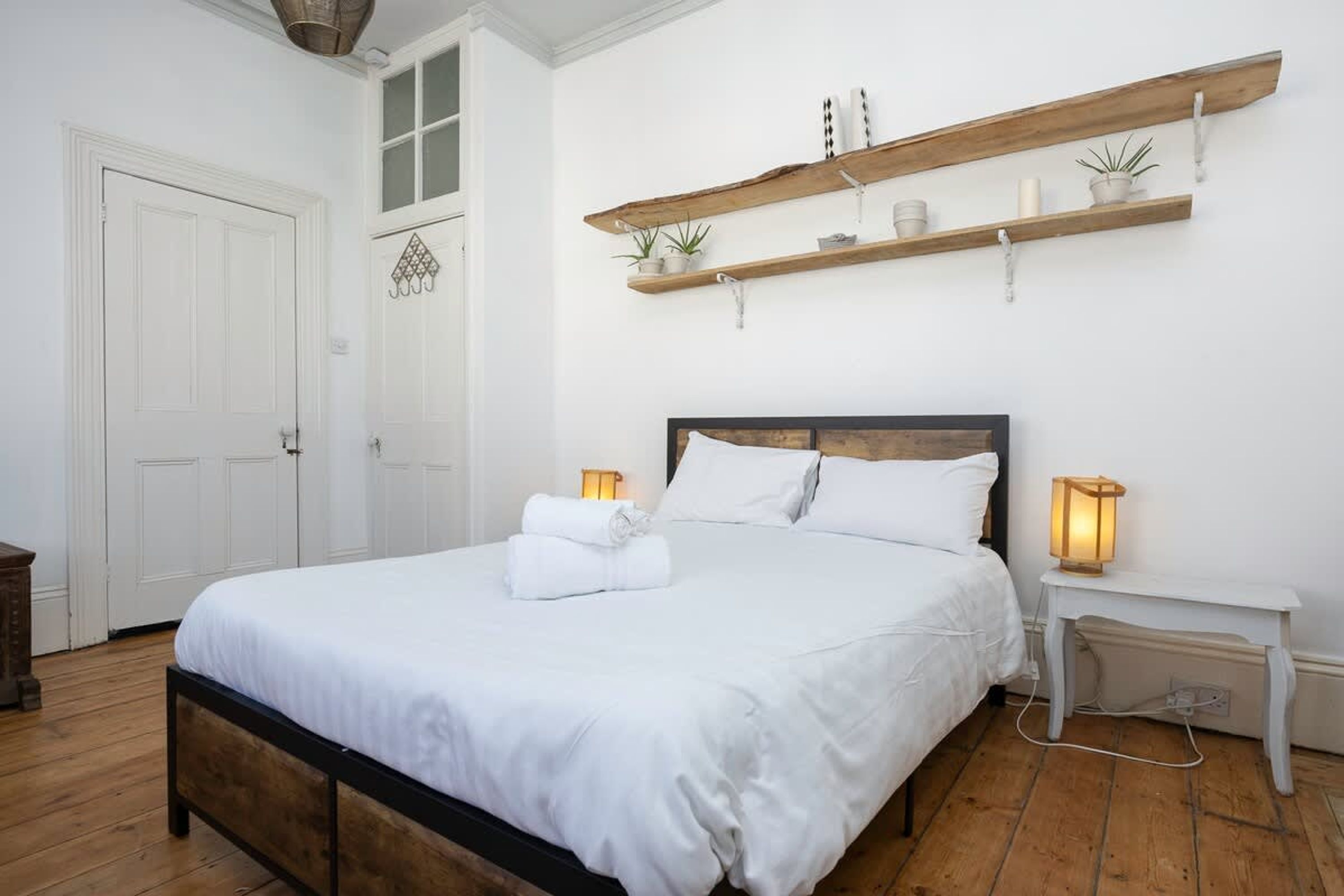 A neatly made bed with white linens, a wooden headboard, and two bedside lamps.