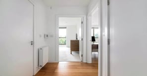 Ein Flur mit weißen Wänden, einem Heizkörper, einem Telefon und einem Holzboden, der zu einem Balkon führt.