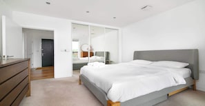 Ein modernes Schlafzimmer mit Bett, Kommode und begehbarem Kleiderschrank.