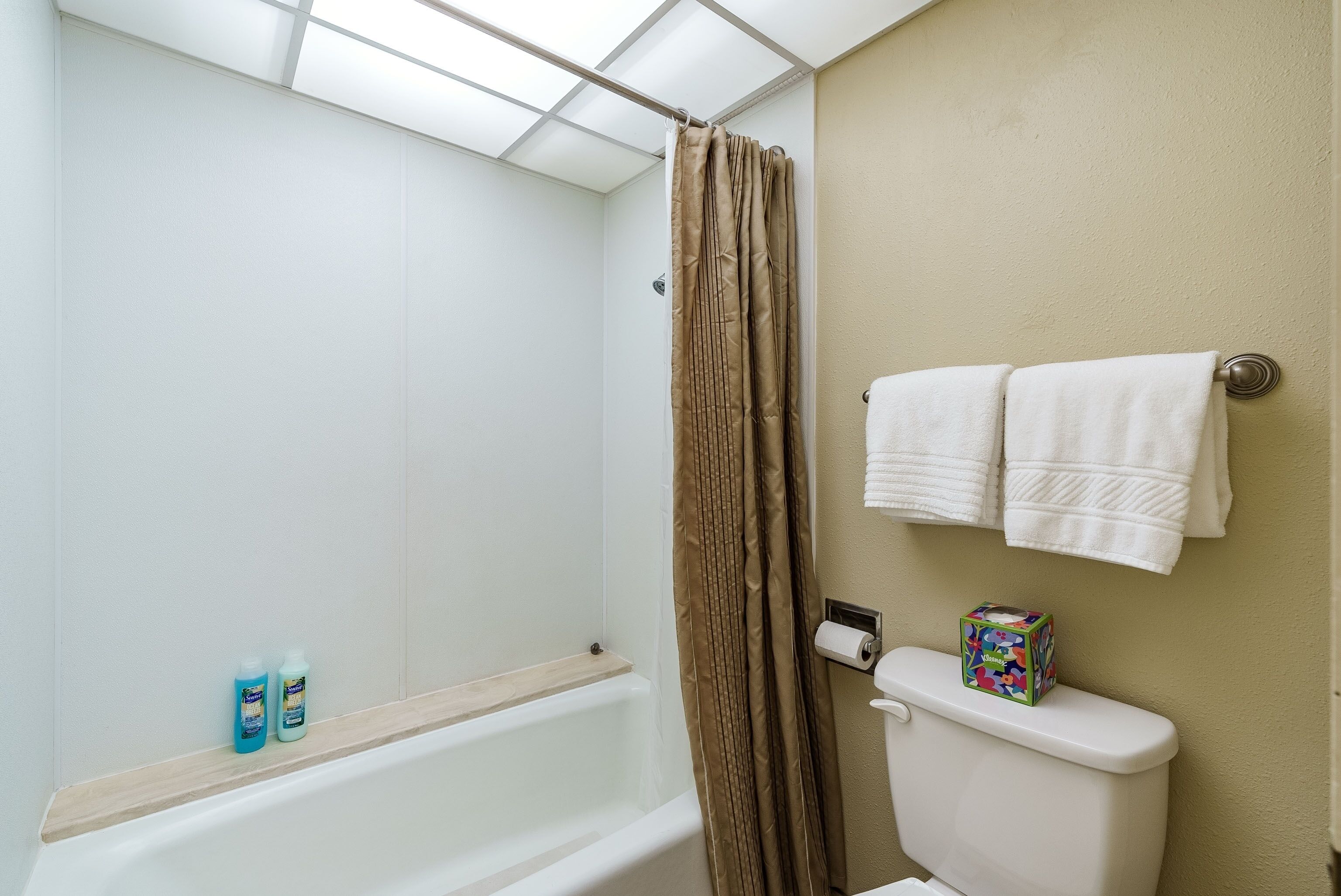 A bathroom with a bathtub, a toilet, and a shower curtain. There are two bottles of liquid soap on the edge of the bathtub.