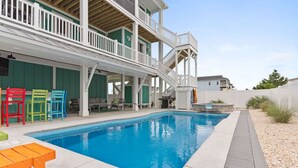 Una piscina con cubierta de madera, sillas de colores y una terraza exterior de varios niveles con barandillas.