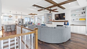 Una cocina moderna con una isla grande, un comedor con sofá seccional gris, y una sala de estar con televisor de pantalla plana.