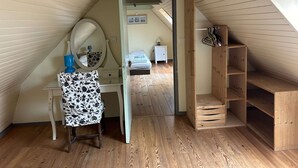 A small attic bedroom with a sloped ceiling, a wooden desk with a mirror, a small bedside table, and a wooden shelf unit. - Kerdraffic Pointe de la Torche (Plomeur)