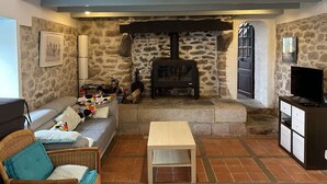 A cozy living room with a stone wall, a fireplace, a sofa, a television, and a wicker chair. - Kerdraffic Pointe de la Torche (Plomeur)