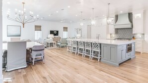 A spacious kitchen with a large island, white cabinetry, and modern lighting fixtures. - Mischievous Mermaid|Easy Beach Access|Private Pool|Game Room|Golf Cart (Seagrove Beach)