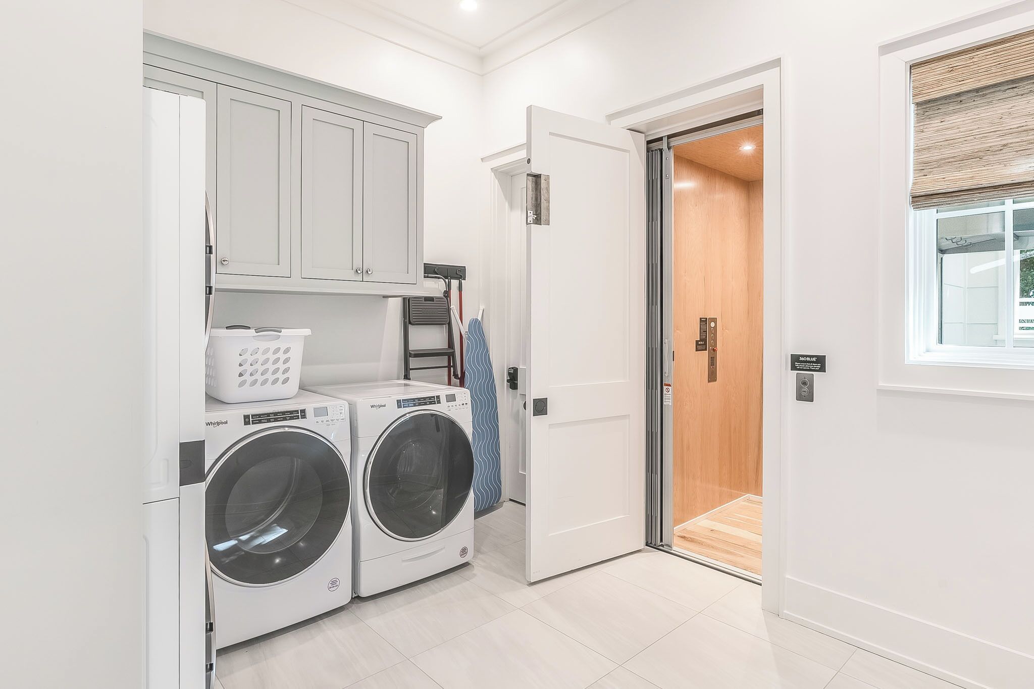 A laundry room with two front-loading washers, a drying rack, and a door leading to a wooden interior.