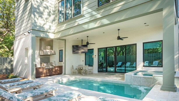 A pool area with lounge chairs, a barbecue grill, and a covered patio with seating and a TV.