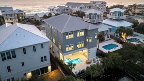 A coastal residential area with multiple houses, a swimming pool, and a view of the ocean at sunset.