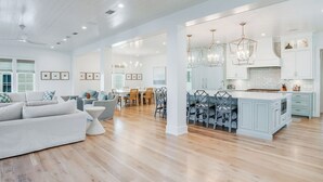 A spacious living area with a large sofa, dining table, and kitchen with light blue cabinets and modern pendant lights.