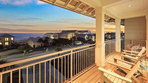 A balcony with wooden railings and chairs, overlooking a residential area with houses and a road.