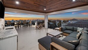 A spacious outdoor patio with a wooden ceiling, a dining area with chairs and a table, and a large sofa with cushions.