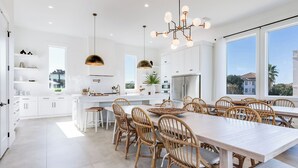 A modern kitchen with white cabinets, a large island, and a dining area with wicker chairs and a long table.