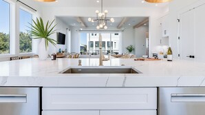 A modern kitchen with a large island, stainless steel appliances, and a central chandelier.