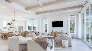 A spacious living room with a large sofa, a dining area, and a TV mounted on the wall.