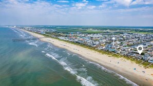 Une vue aérienne d’une ville côtière avec une plage, des maisons et une jetée qui s’avance dans l’eau.