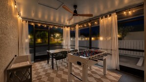 Eine gemütliche Terrasse im Freien mit einem Tischkicker, einem Deckenventilator und Lichterketten.