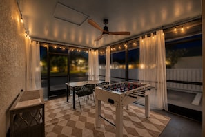A cozy outdoor patio with a foosball table, a ceiling fan, and string lights.