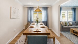 Ein Essbereich mit Holztisch, gedeckt für vier Personen, einem Kronleuchter und einem Sofa im angrenzenden Wohnzimmer.