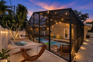 Un espacio al aire libre con paredes de cristal, piscina, asientos e iluminación con guirnaldas.