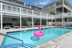 A swimming pool with a pink flamingo float, lounge chairs, and a covered deck area.