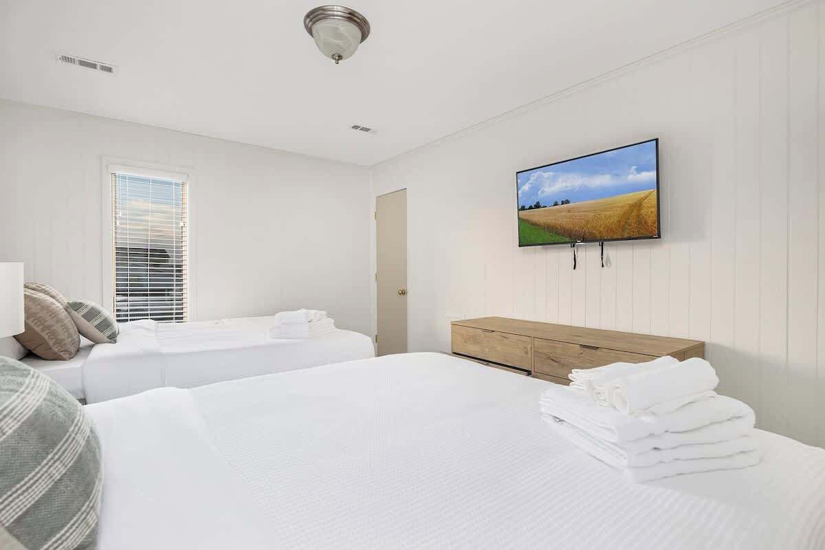 A hotel room with two beds, a wooden dresser, a flat-screen TV, and a window with blinds.