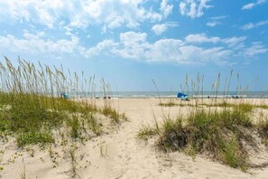 Ein sandiger Pfad am Strand, der zum Meer führt, mit Dünen an beiden Seiten.