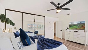 A bedroom with a bed, a TV, a dresser, a ceiling fan, and a large window.