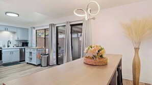 A modern kitchen with light blue cabinets, a wooden countertop, and a dining area with a vase of flowers.