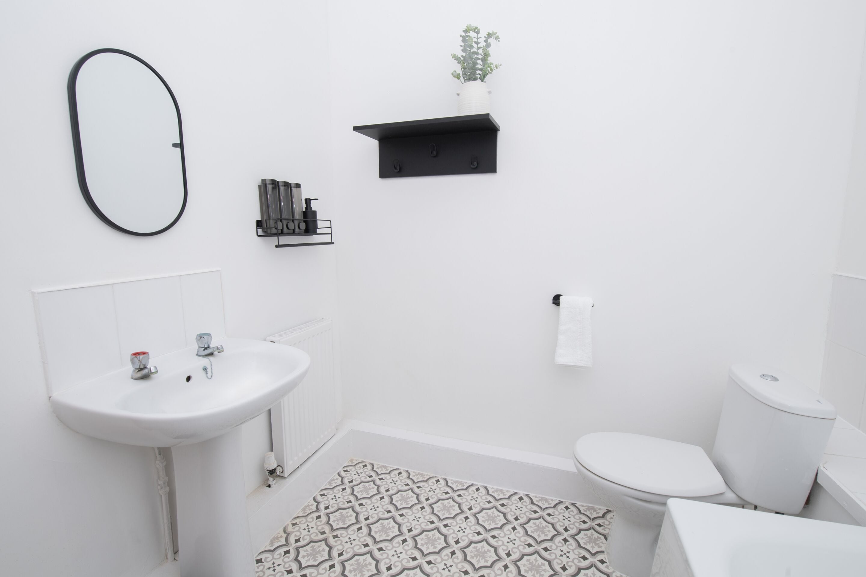 A modern bathroom with a white sink, toilet, and a patterned rug.