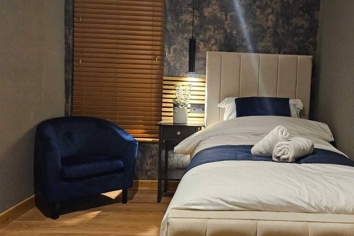 A bedroom with a bed, a chair, a nightstand, and a window with blinds.